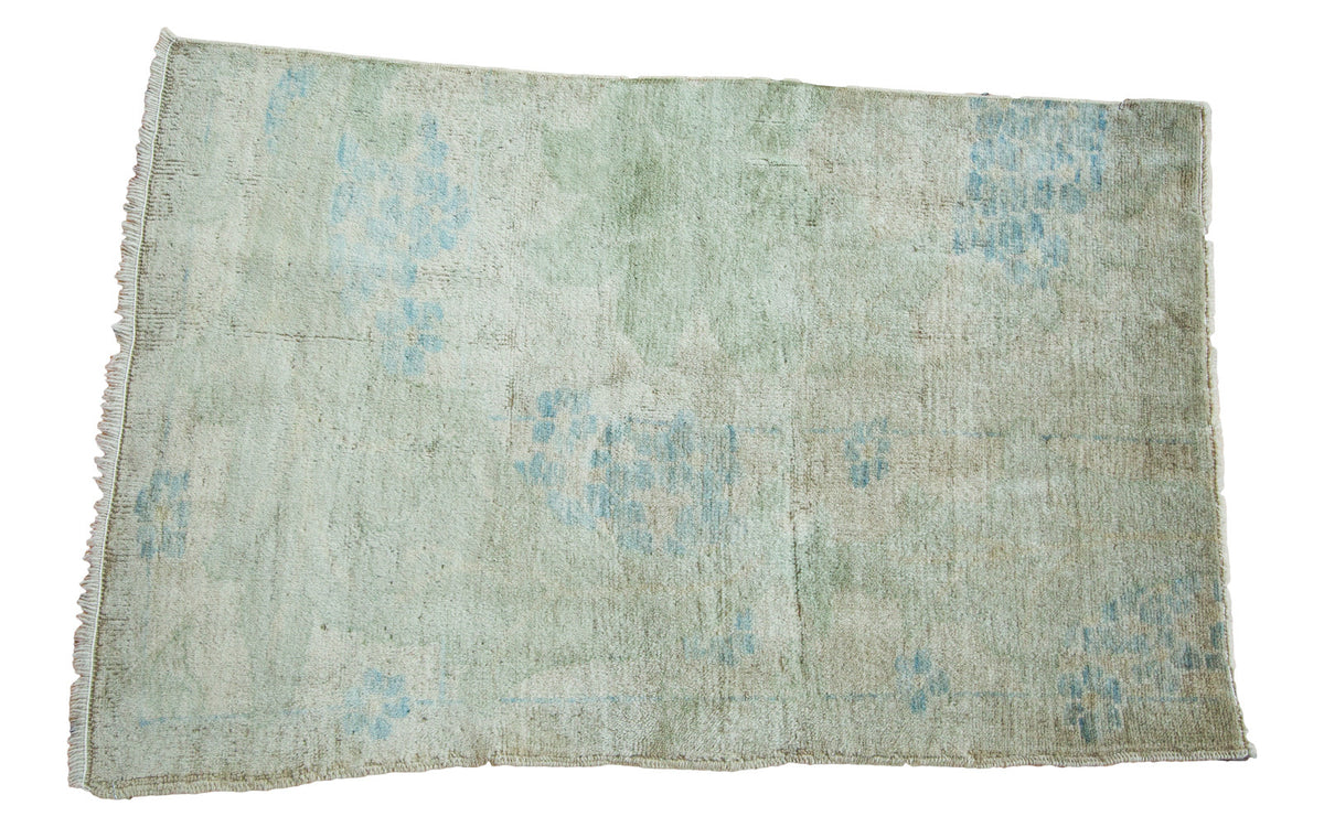 Distressed vintage Oushak rug featuring faded light blue plant motifs on a light green field.