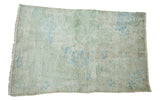 Distressed vintage Oushak rug featuring faded light blue plant motifs on a light green field.
