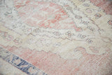 Distressed texture of a vintage Oushak rug showing faded pink and cream patterns.