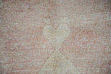 Detail of worn pile and visible foundational weave on a distressed Oushak rug in beige and muted red.