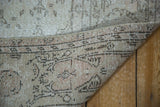 Distressed Oushak carpet folded, showcasing blanched ivory pile and woven backing.