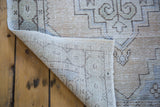 Curled distressed Oushak runner revealing hand-knotted back and beige, ivory, charcoal geometric pattern.