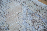 Textured distressed Oushak rug surface with geometric motifs in beige and soft blue.