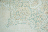 Blanched green, ivory, and tan curvilinear motif on a distressed Oushak rug.