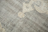 Distressed Oushak carpet texture showing blanched ivory, beige motifs on charcoal.