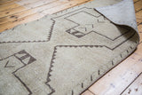 Rolled corner of a distressed Oushak runner, revealing its hand-knotted back and geometric pattern.