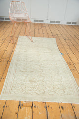 Corner view of distressed blanched Oushak rug, showing faint scrolling vines pattern.