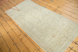 Distressed blanched Turkish Oushak rug corner, showing scrolling vine pattern and fringe.