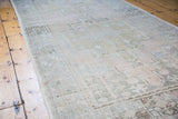 Distressed Oushak rug detail with soft apricot, charcoal, and muted green geometric motifs.