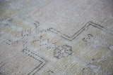 Close-up of distressed Oushak rug showing soft gold, charcoal geometric lines and apricot field.