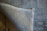 Distressed Oushak rug's hand-knotted foundation, fringe, and muted geometric texture in soft tones.