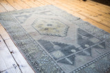 Angled view of distressed Oushak rug shows muted apricot, gold, and charcoal geometric pattern.