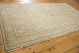 Distressed Oushak rug corner showing faded curvilinear motifs in silver, ivory, and brown.