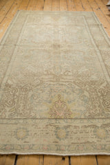 Close-up of distressed Oushak palmette medallion with muted ivory, pale blue, and brown shadows.