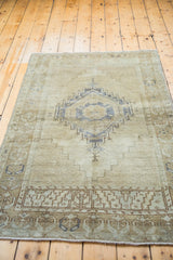 Distressed Oushak rug corner featuring muted silver geometric medallion and patterned border.