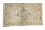 Distressed vintage Turkish Oushak rug with silver medallion, meandering border, soft beige and gold.