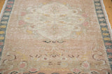 Blanched distressed texture of a vintage Oushak rug, showing faded pastel pink and yellow hues.