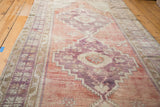 Distressed Oushak runner, showcasing thin pile, faded violet and peach geometric medallion.