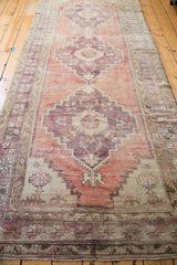 Distressed Oushak runner's geometric medallion with thin pile and sun-softened violet-red.