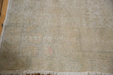 Distressed Oushak rug detail, showing hand-knotted weave, pale ivory, grey, soft rose hues, and fringe.