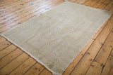 Distressed Oushak rug corner, faded ivory pile texture with soft rose accents.