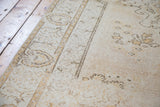 Thin pile texture of distressed Oushak rug with soft saffron gold motifs and neutral field.