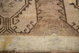 Detail of distressed Oushak rug, geometric brown patterns, soft beige pile, and ivory border.
