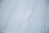 Close-up of vintage dhurrie flatweave texture, bleached ivory, with subtle stripes and sewn seam.