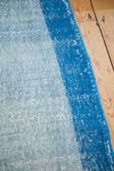 Distressed light and dark blue Oushak runner showing low pile and narrow border.