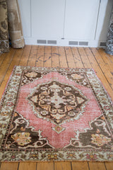Distressed deep rose field with ivory and charcoal bronze patterned border on a vintage Oushak rug.