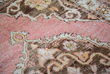 Distressed rose Oushak rug, highlighting worn texture and faded charcoal bronze motifs.