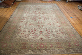 Corner of vintage Oushak carpet with distressed rosey red floral motifs and wooded borders.