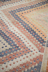 Geometric zig-zag and diamond patterns on a vintage Jajim rug in orange, red, and blue.