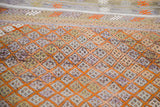 Distressed Jijim rug detail with tangerine orange diamond grid on multi-tonal hand woven squares.