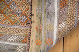 Distressed Jijim rug detail: vibrant hand woven texture with tangerine, ivory, and silver earth tone motifs.