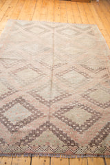 Vintage Jijim carpet's geometric medallions in sea foam, grapefruit, aubergine, showing fringe.