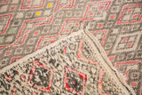 Folded vintage Jajim rug edge detailing its geometric pattern with soft charcoal, tangerine, red.