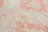 Vintage Jijim carpet detail with geometric guls, ivory and faded cinnabar tones, showing loose fibers.