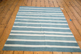 Corner view of a hand woven kilim rug with striated sky blue and ivory flatweave.