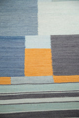 Abstract geometric blocks and striped bands in shades of blue, charcoal, and saffron gold kilim.