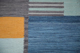 Hand woven kilim detail showing abstract geometric blocks, saffron gold, charcoal, and blue stripes.