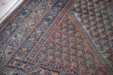 Distressed vintage Mir Serbend rug corner, showcasing faded coral and deep blue patterns.