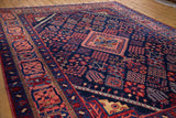 Dense wool of a vintage Joshegan carpet: jewel-toned indigo field, salmon border, varied floral motifs.