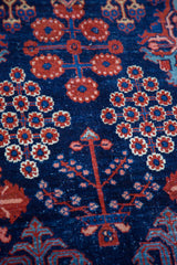 Hand-knotted pile showing blossoming tree and flower motifs in indigo and ruby tones.