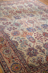 Distressed Kazvin carpet close-up, showing Safavid palmettes, vines, and blossoms in beige, ruby, and navy tones.