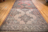 Distressed Oushak runner with ornate geometric medallions in a worn rose, grey, and brown palette.