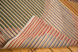 Folded New Kilim rug revealing abstract striated green, beige, red, and gray patterns.