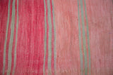 Textured handwoven kilim weaving featuring striped bands of pale rose, cinnabar, and grey.