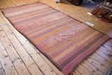 Fringed end of the vintage Kilim carpet, with striated bands in faded tangerine, rose, and mauve.