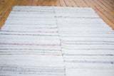 Vintage rag rug close-up showing white, grey, blue flatwoven stripes and central seam.